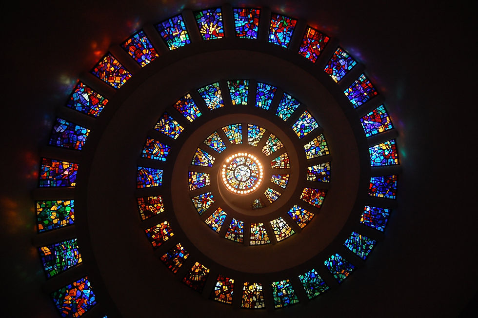Spiral staircase ceiling with concentric stained-glass windows in blue, red, and gold around a glowing central light.