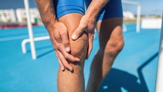 A male runner holding the front of his knee due to pain.