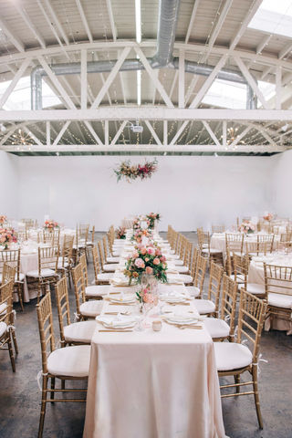 Long wedding tables with gold chiavari chairs in a modern studio space with low floral centerpieces. 