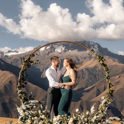 Couple standing beneath floral hoop arch at mountain proposal in the Sacred Valley, surrounded by Andean peaks.