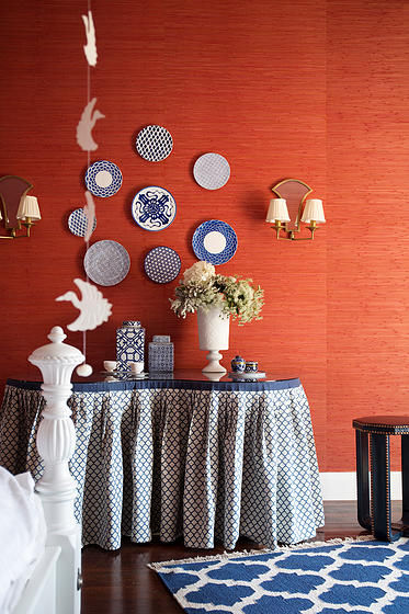 Vibrant orange grass wallpaper against a backdrop of navy blue and white textiles, evoking Moroccan charm in eclectic interior design.