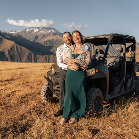 Couple embracing beside jeep after mountain proposal in the Sacred Valley, Andes Mountains of Peru.