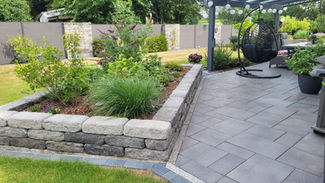 Terrasse mit Hochbeet und Pflanzen im Hintgergrund eine Gartenmauer und Sichtschutzelemente