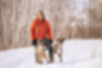 A woman poses with her two dogs in the snow.