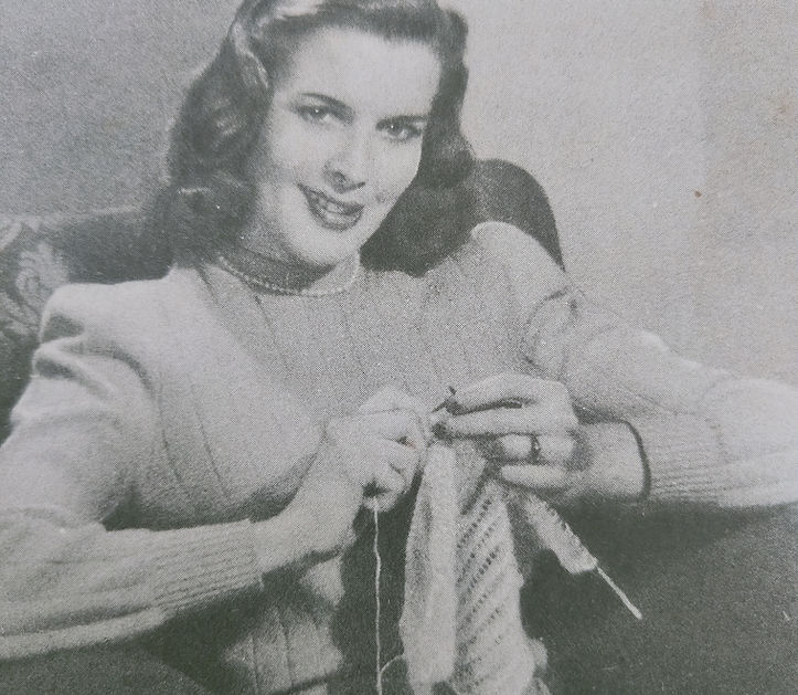 A black and white images of a seated lady knitting  and wearing 1940s handknit sweater and purls