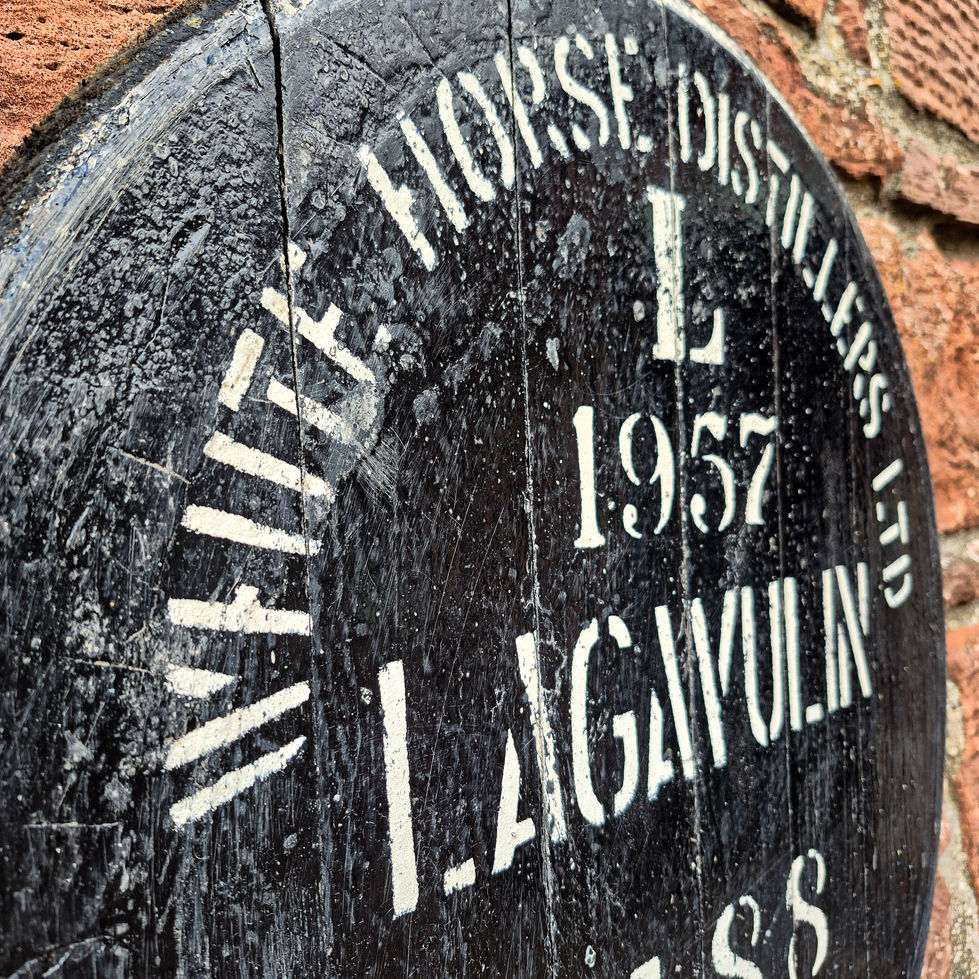 Cropped angled close-up of a black Lagavulin 1957 whisky barrel cask head stamped White Horse Distillers.