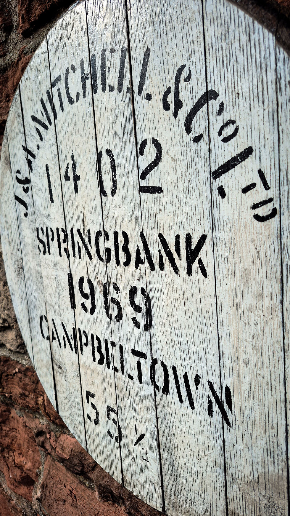 Close-up of a Springbank 1969 whisky cask head showing stencilled lettering on weathered white oak staves.