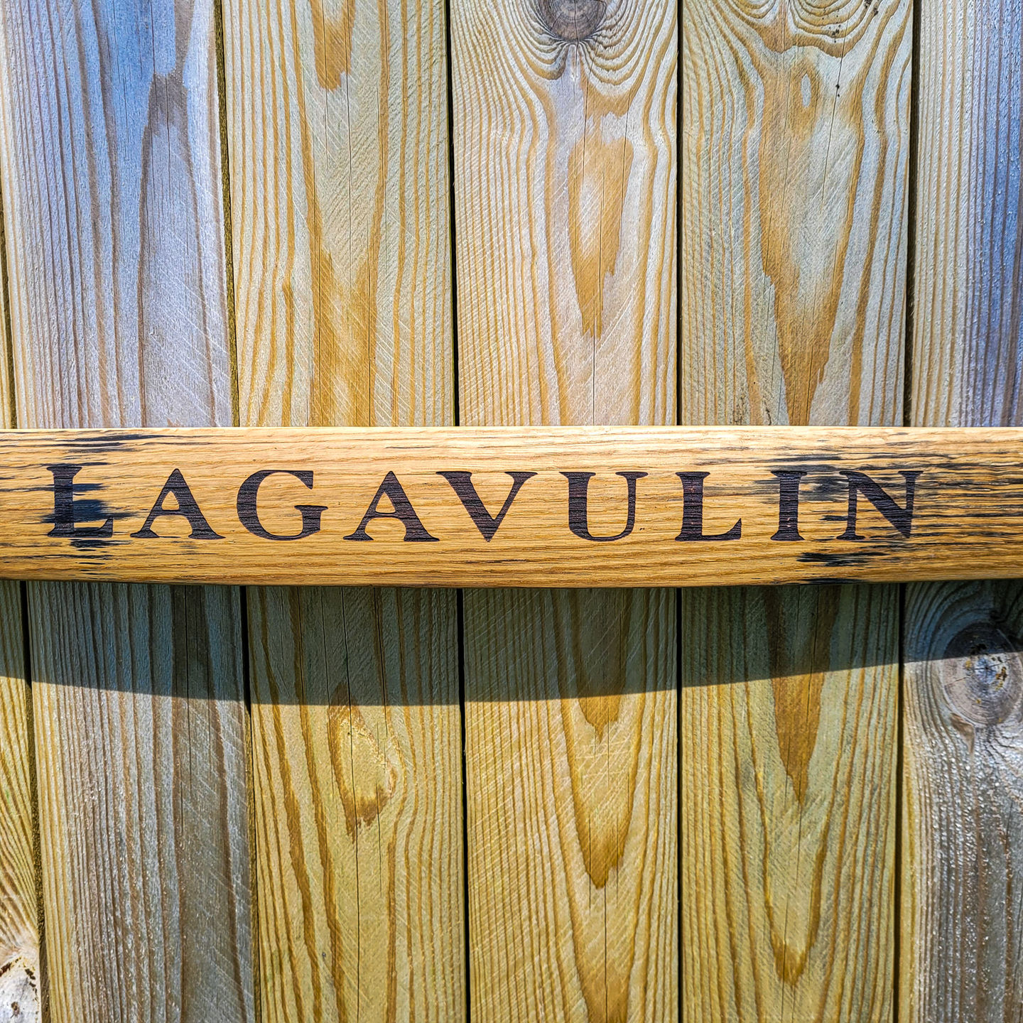 Whisky barrel stave sign Lagavulin distillery branding on reclaimed Islay oak with warm amber tones mounted on wooden fence