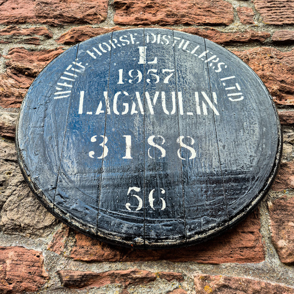 Low angle of a black Lagavulin 1957 whisky barrel cask head stamped White Horse Distillers on a stone wall.