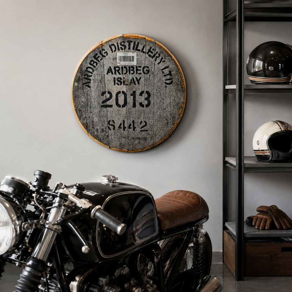 Reclaimed Ardbeg Distillery whisky barrel cask head wall art mounted on a gray wall behind a vintage motorcycle.