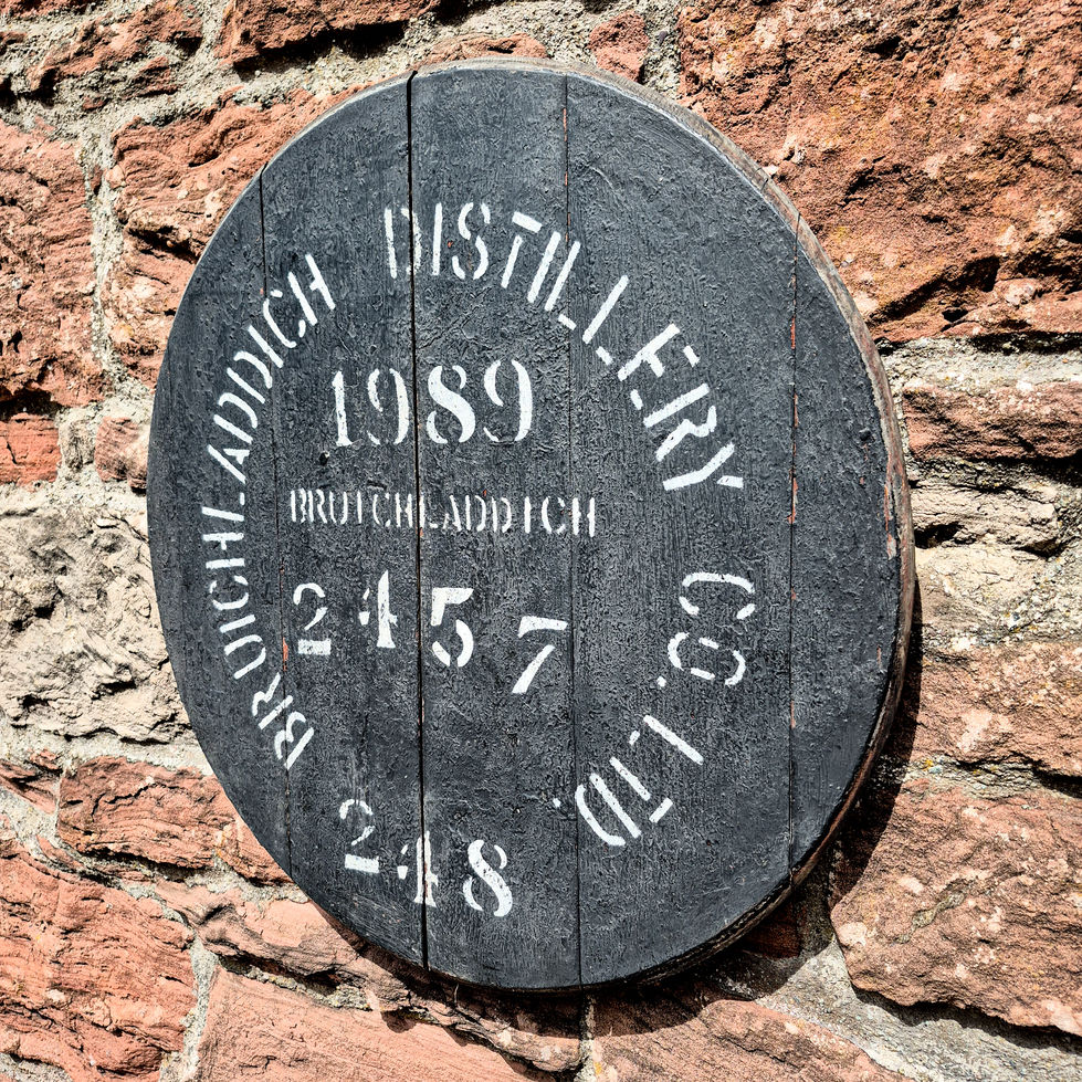 Angled close-up of a black Bruichladdich Distillery 1989 whisky barrel cask head on a stone wall.