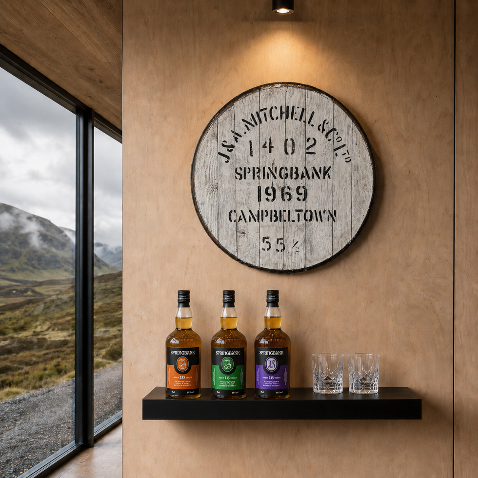 Springbank 1969 whisky cask head wall art above a shelf with three bottles and glasses by a window with mountain views.