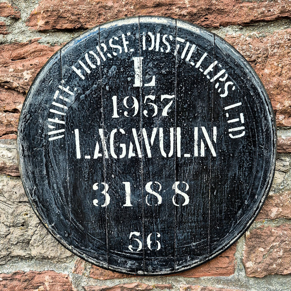 Close-up of a black whisky barrel cask head stamped White Horse Distillers and Lagavulin 1957 on a stone wall.