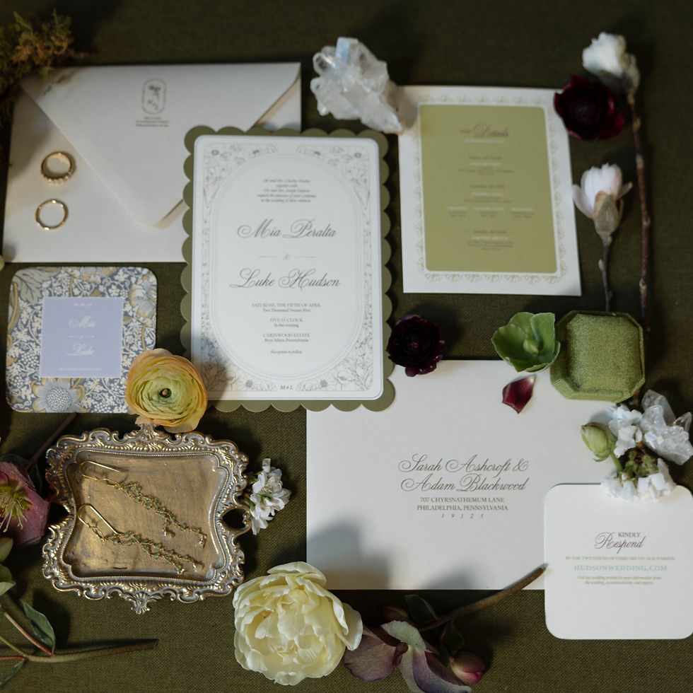 Elegant wedding invitations and envelopes on a dark surface, surrounded by flowers and jewelry. Text includes names Moira and Luke.