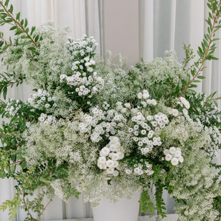 White floral wedding arrangement in modern vase with greenery and neutral drape backdrop