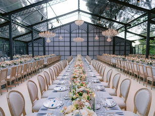 Long wedding reception tables with florals under glass atrium at garden wedding venue