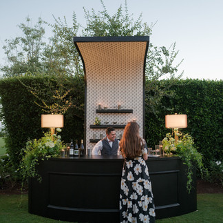 Black bar with curved arch, backlit pattern wall and floral accents at luxury outdoor event