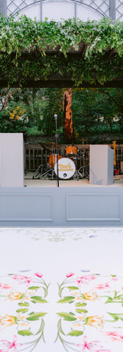 Wedding stage with floral-patterned dance floor and greenery canopy at garden venue