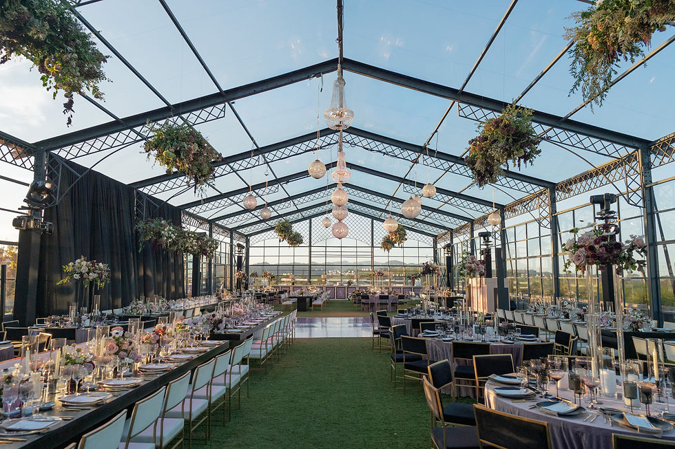 Tented wedding reception setup with chandeliers and greenery overhead.