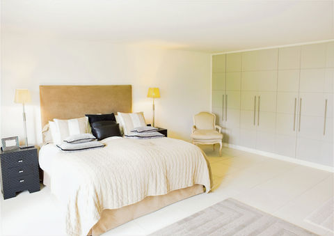 Elegant bedroom with a plush upholstered bed, built-in wardrobe, warm ambient lighting, and neutral-toned decor.