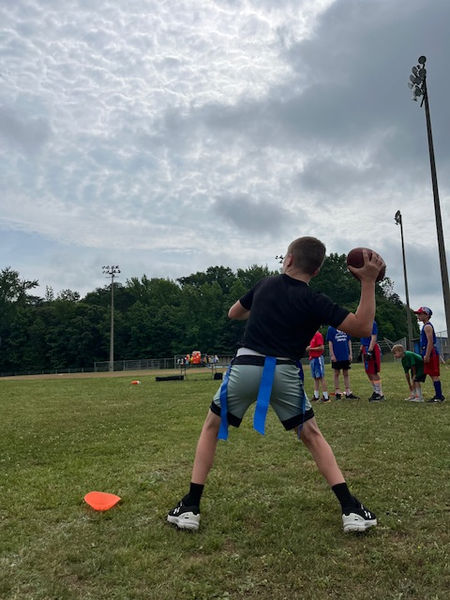 Young person in black shirt throwing football during flag football game.