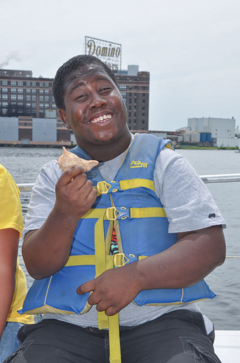 Happy young man eating pizza slice, Stearns life vest, waterfront.