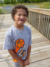 Young boy in sports t-shirt, missing teeth, on wooden boardwalk.