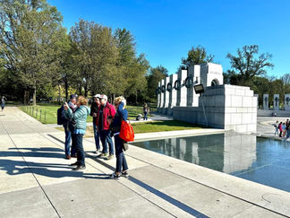 Group standing by World War II Memorial reflective pool, sunny day.