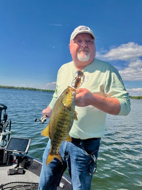 Man holding a fish, clear sky and open water on a sunny day.