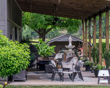 Covered outdoor patio with dining set, fountain, and lush green plants.