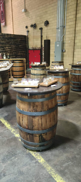 Whiskey barrel tables with tasting glasses arranged for a distillery event.