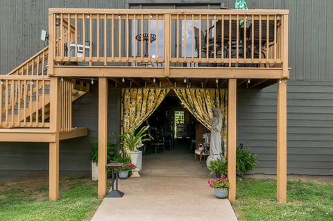 Building entrance with yellow floral curtains, plants, and second-story deck.