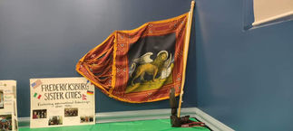 Ornate red and gold flag with winged lion, leaning against blue wall.