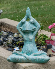 Teal green frog garden statue meditating in a yoga pose outdoors.