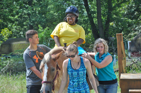 Therapeutic horseback riding for smiling young woman with three helpers.