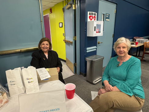 Two smiling women at event table, with "Sweet Deal!" and "AED".