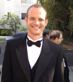 Smiling man wearing a black tuxedo, bow tie, and vest at event
