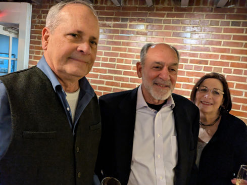 Two men and one woman smiling at an event against brick wall.