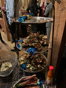 Three-tiered display of baked oysters with blue orchids and hot sauce.