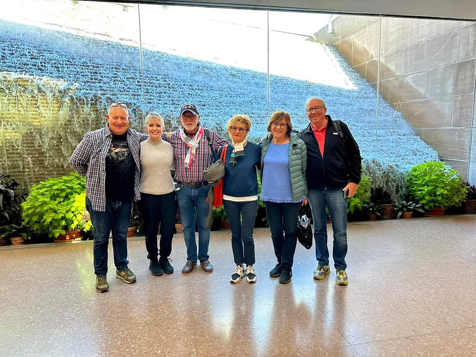 Six adults posing together indoors beside a large plant wall.