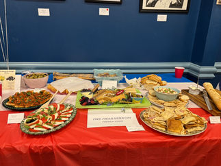 Potluck table spread with various dishes and a "FRED. SISTER CITY" sign.