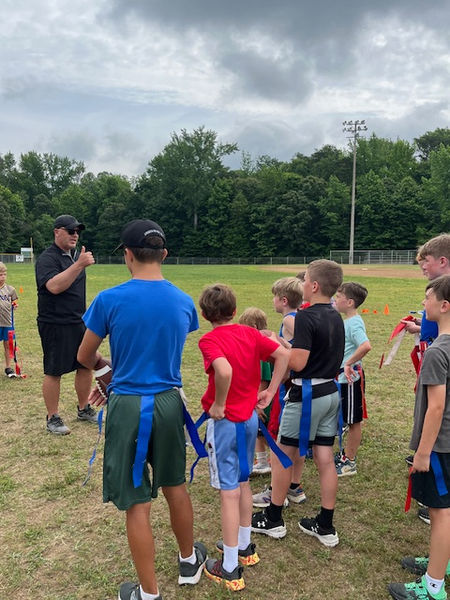 Adult coach instructing young boys at flag football practice outdoors.