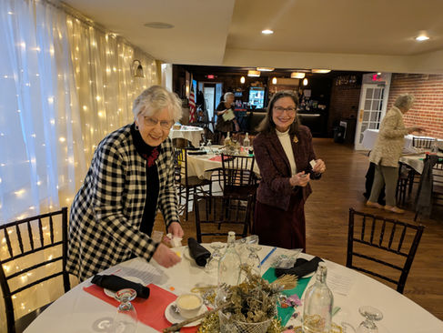 Two women prepare a decorated dining table for an indoor event.