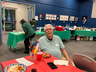 Smiling elderly man at red table with international flags, food, and drink.