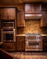 Rustic kitchen with dark wood cabinets, stainless microwave, oven, and range.