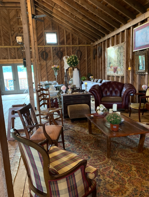 Rustic barn interior with lounge furniture, dining tables, and floral decorations.