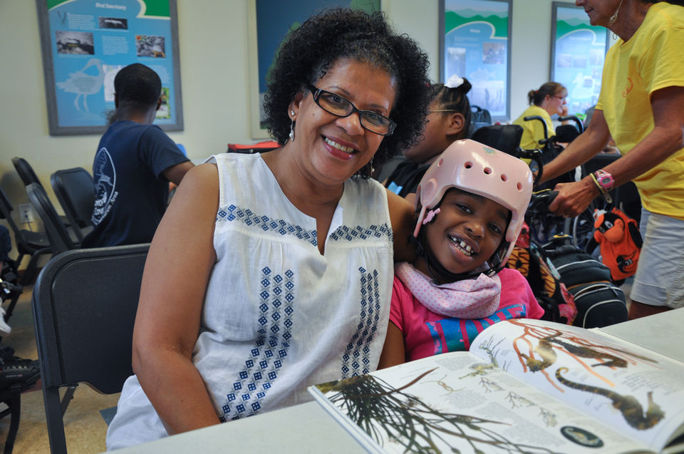 Smiling woman and child wearing pink helmet reading book together