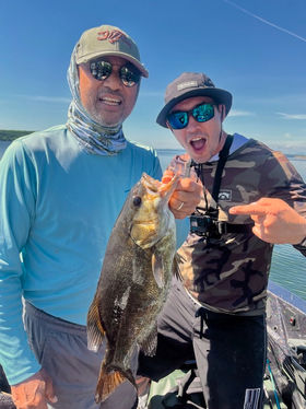 Two men proudly display a freshly caught fish against a scenic backdrop.