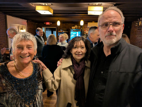 Three smiling individuals posing together at an indoor gathering.