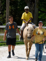 Young man and woman assisting smiling rider on palomino horse.